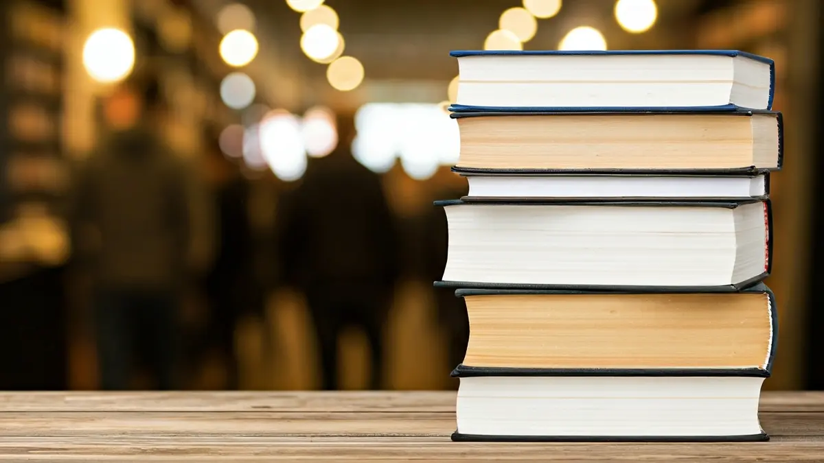 Generic image of books stacked on a wooden table, with a blurred library background.