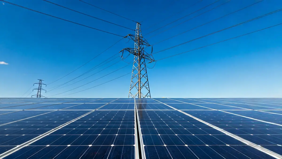 Imagen genérica de una torre eléctrica con paneles solares al fondo, simbolizando la transición energética.