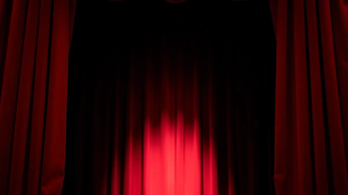 Imagen genérica de un escenario de teatro con cortinas de terciopelo rojo, sugiriendo una representación.