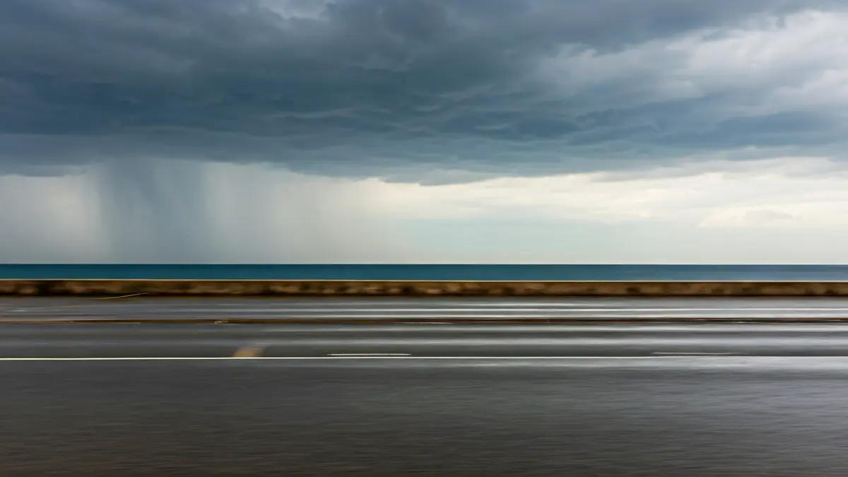 Imagen genérica de un paisaje costero mediterráneo bajo un cielo gris y tormentoso, con lluvias intensas y un charco de barro.