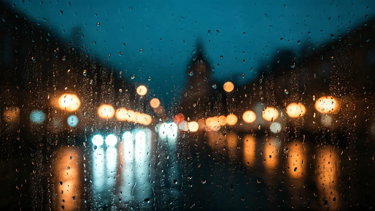 Imatge genèrica de pluja caent sobre un vidre amb llums de ciutat desenfocades al fons.