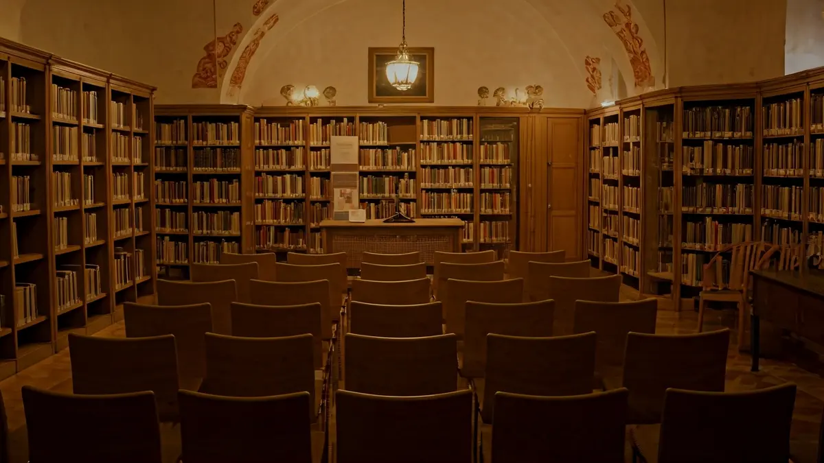 Imagen genérica de un interior de biblioteca con estanterías de madera y un atril con micrófono.