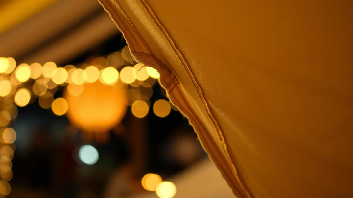 Image of a torn fallas tent canvas, with blurred festive lights in the background.
