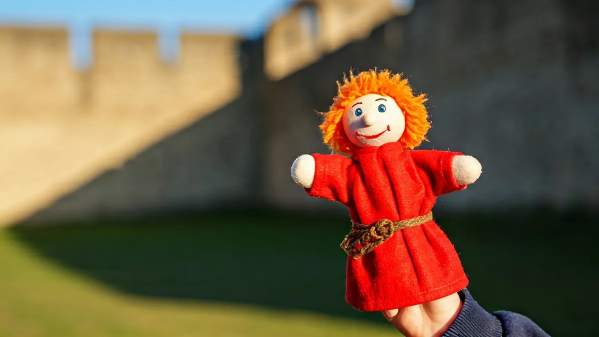 Imatge d'un titella de dit en una mà infantil amb un castell antic de fons.