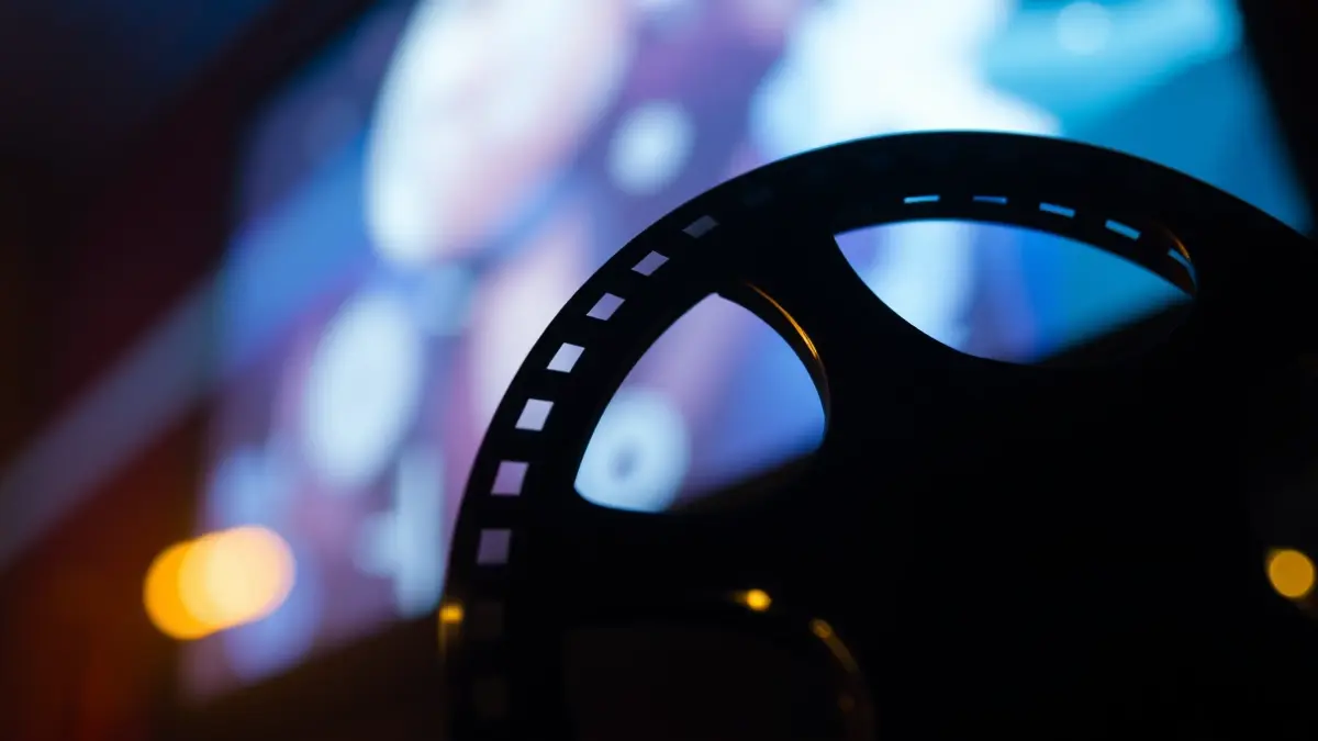 Generic image of a film reel with blurred lights of a cinema screen in the background.