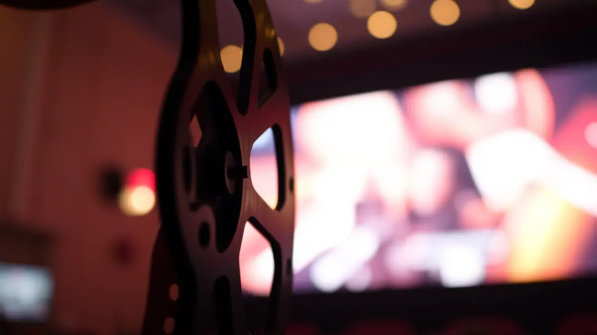 Imagen genérica de un carrete de película con luces borrosas de una pantalla de cine al fondo.
