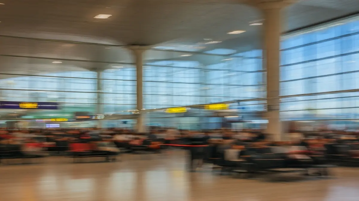 Generic image of an airport interior with blurred passengers and large windows.