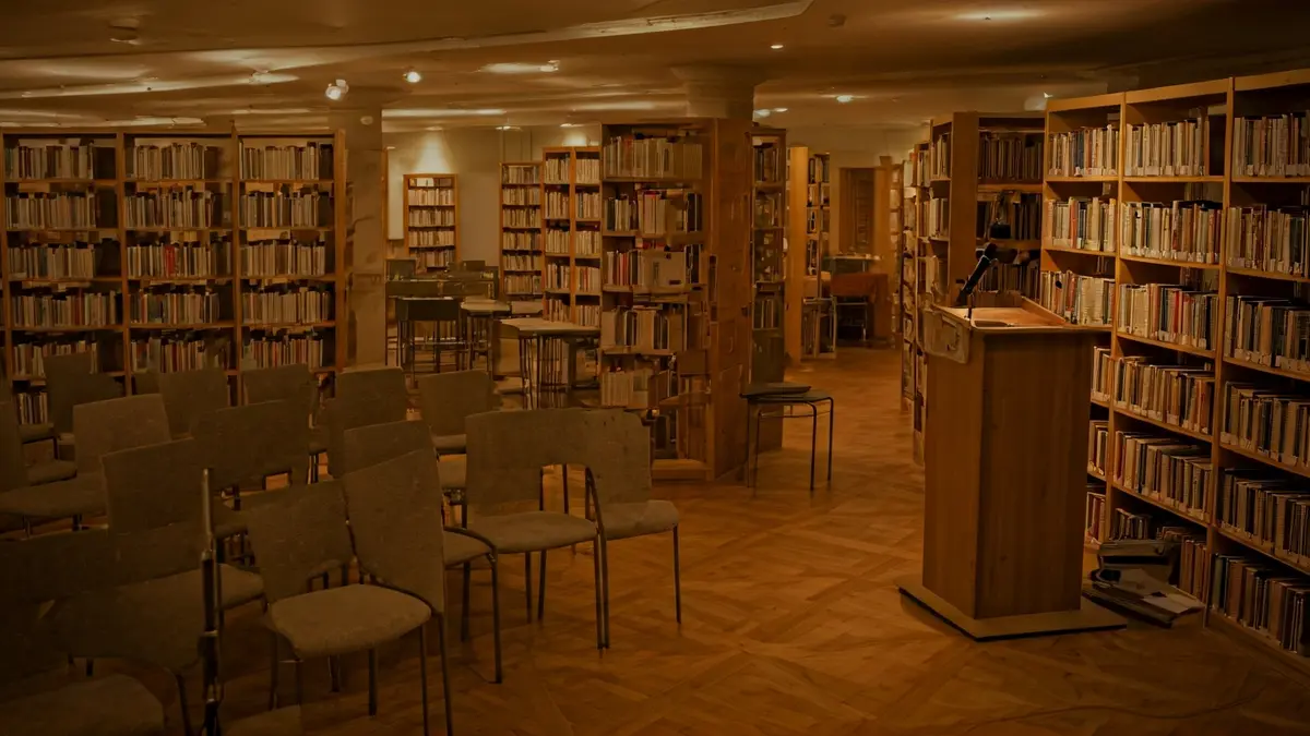 Imagen genérica de un interior de biblioteca con estanterías de madera y un micrófono en un podio.