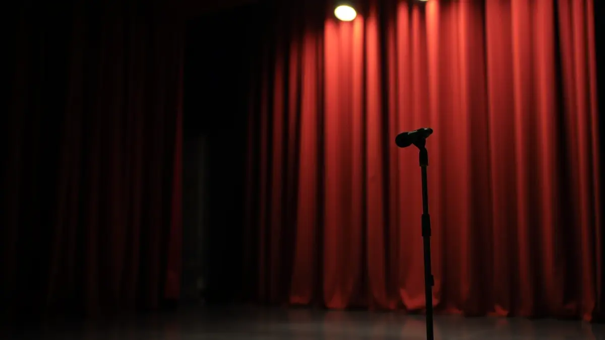 Imagen genérica de un escenario teatral vacío con un foco, cortinas borrosas e iluminación cálida.