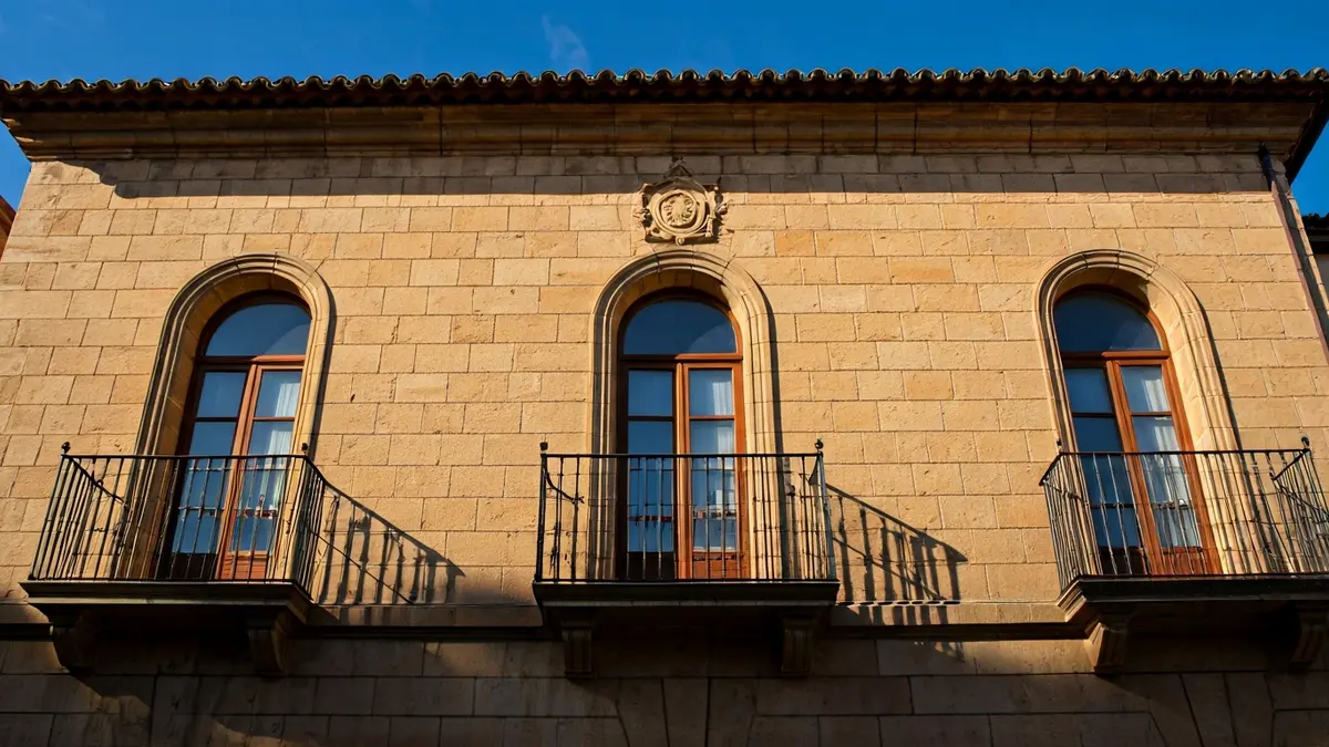 Imagen de la fachada de un ayuntamiento de piedra con balcón y barandillas de hierro