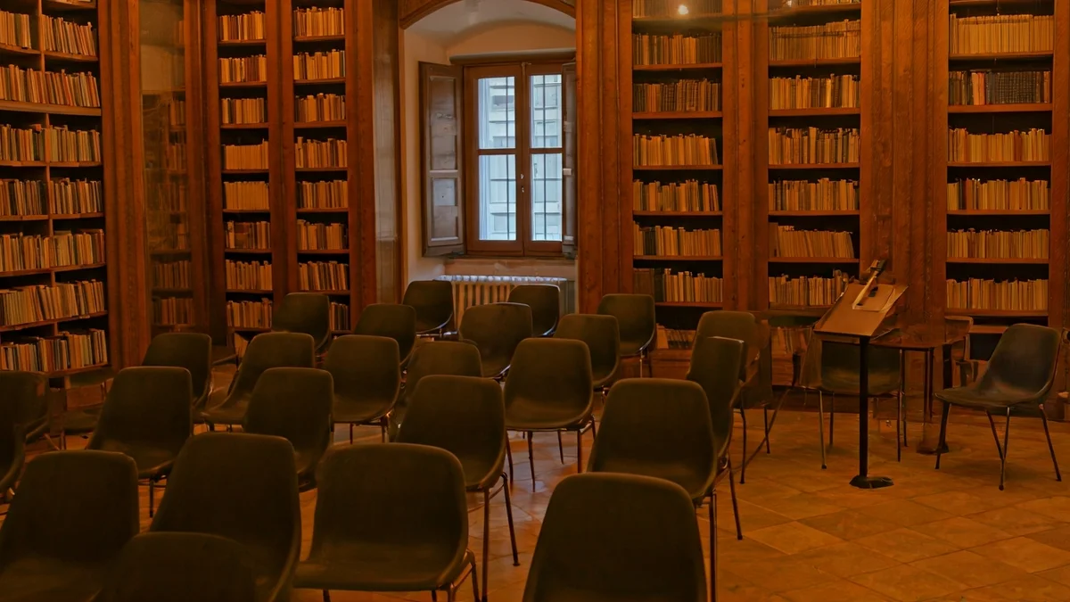 Imagen genérica de un interior de biblioteca con estanterías de madera y un atril con micrófono, iluminación cálida.