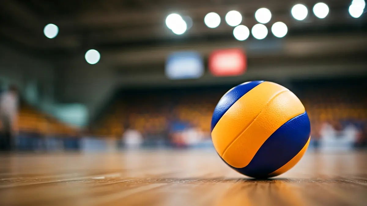 Imagen genérica de un balón de voleibol en una cancha de madera, con un fondo borroso de un pabellón deportivo.