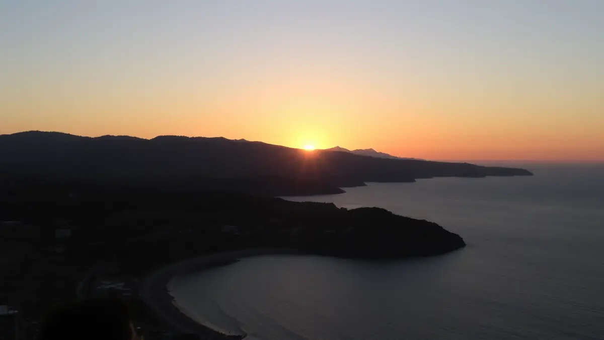 Imatge d'un eclipse solar parcial en un paisatge costaner mediterrani al capvespre, amb el sol baix en l'horitzó.