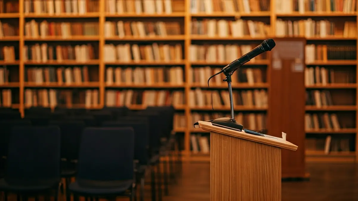 Imatge genèrica d'una biblioteca amb prestatgeries de fusta i un faristol amb micròfon, amb una il·luminació càlida.