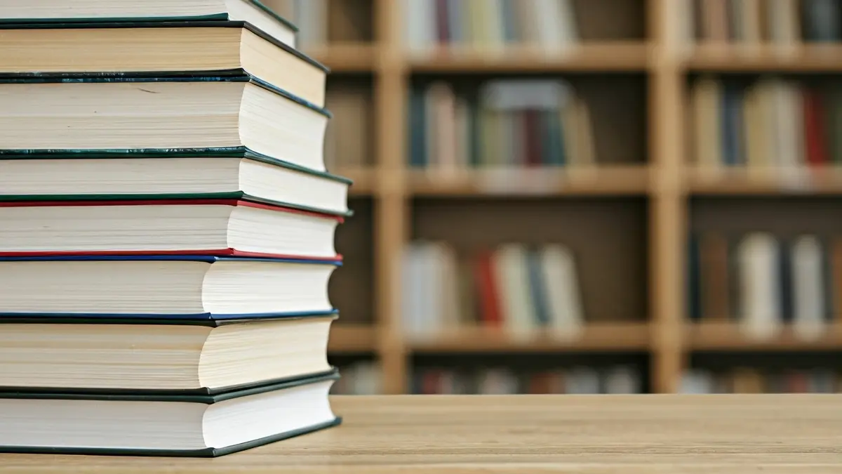 Imagen genérica de libros sobre una mesa de madera, con un fondo desenfocado de una biblioteca o aula.
