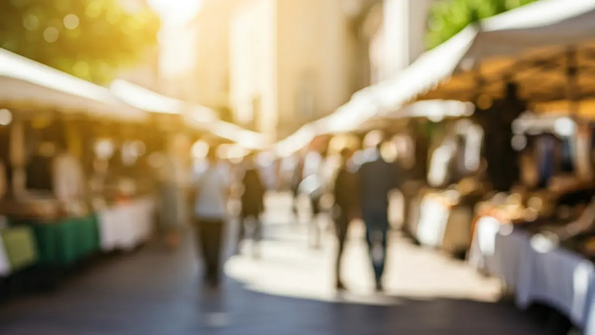 Imatge genèrica d'una fira de comerç local en una plaça mediterrània, amb parades i gent passejant.