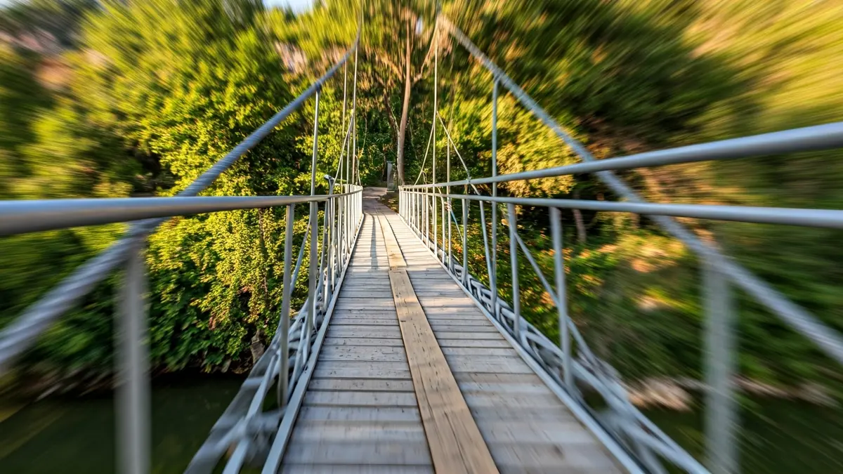 Image of a temporary pedestrian bridge over a river, with Mediterranean vegetation on the banks.