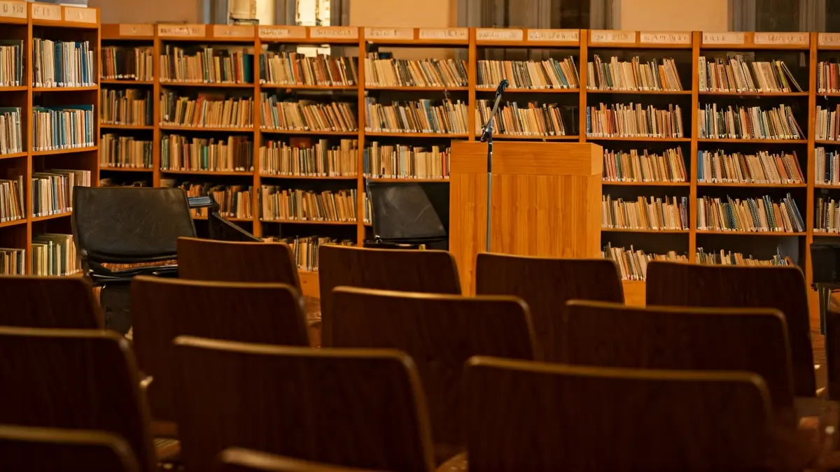 Imagen genérica de un interior de biblioteca con estanterías de madera y un atril con micrófono.