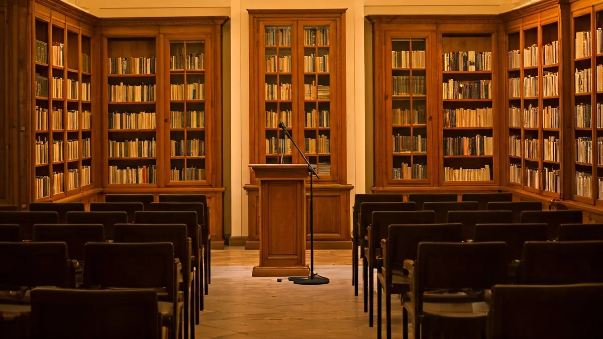 Generic image of a conference room or library with a podium and empty chairs, warmly lit.