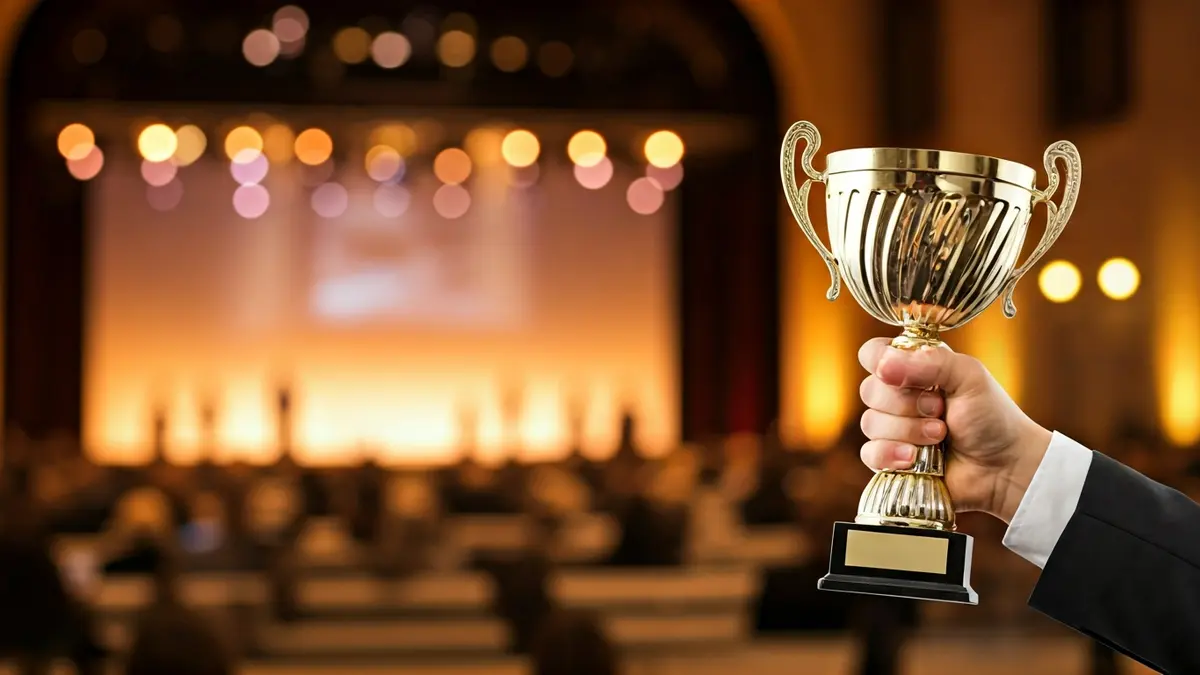 Imagen de una mano sosteniendo un trofeo en una ceremonia de premios, con figuras borrosas al fondo.