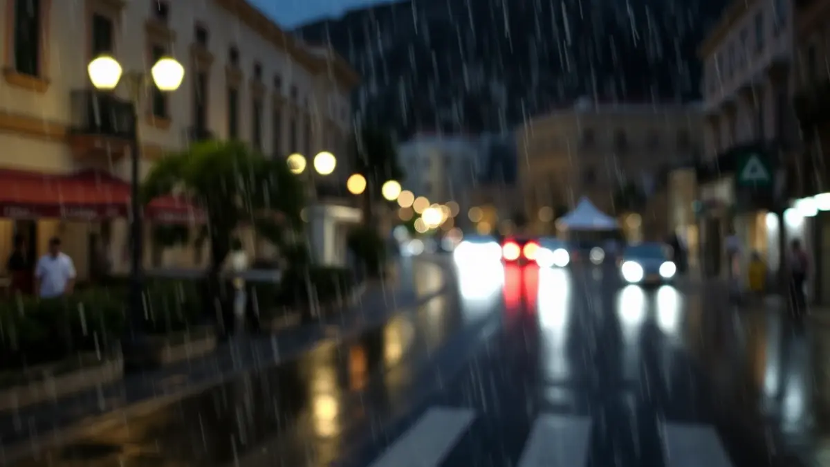 Imagen genérica de lluvia en una calle de una ciudad mediterránea, con edificios y farolas borrosas.