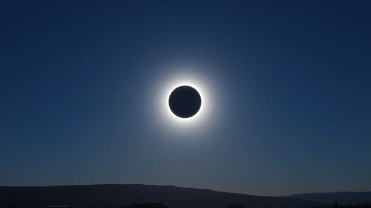 Imagen de un eclipse total de sol, con el cielo oscuro y una corona alrededor del sol oculto. Sin edificios ni personas.