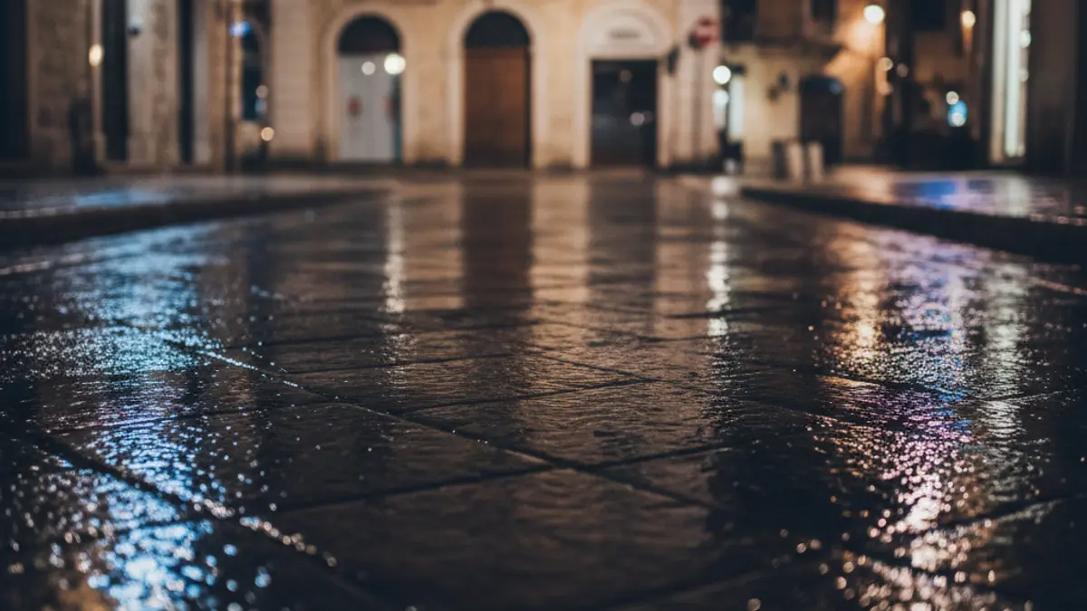 Imatge genèrica de llums d'emergència reflectint-se en l'asfalt mullat de nit, sense vehicles visibles, en un entorn urbà mediterrani.
