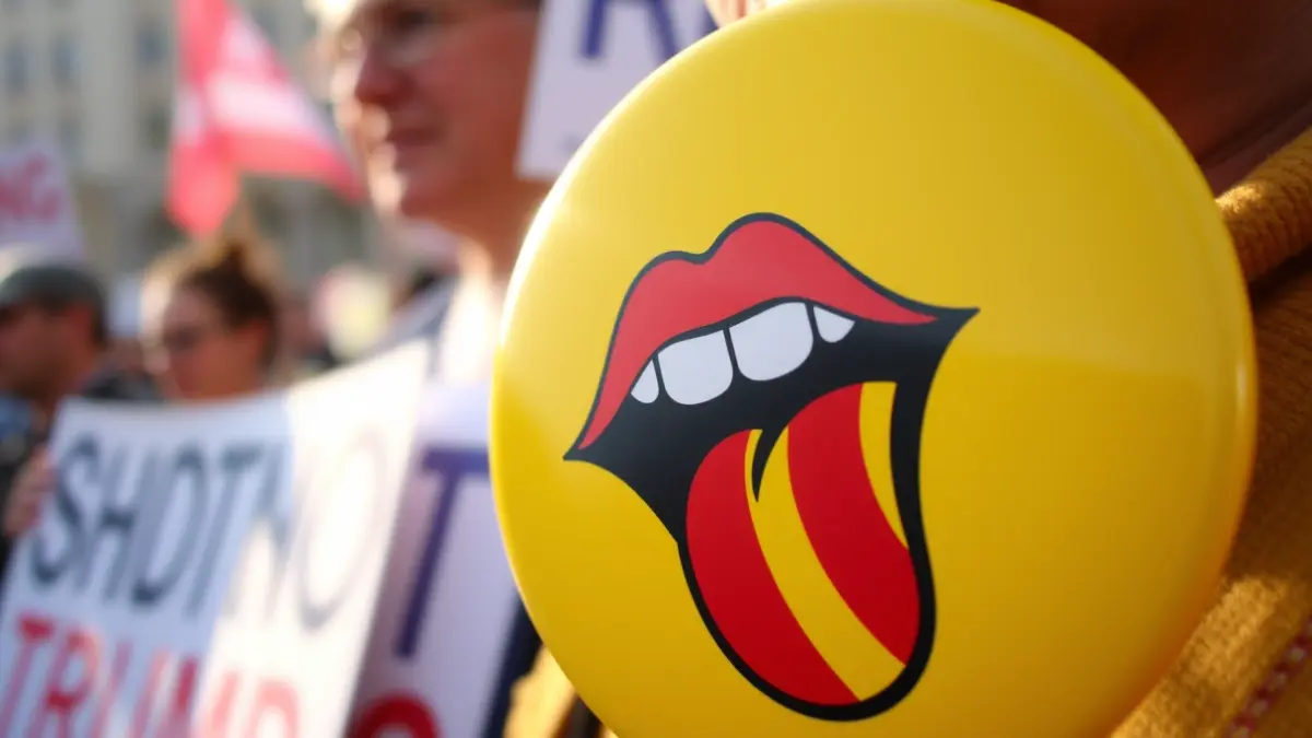 Imagen de una pegatina con una boca y una lengua con las cuatro barras, símbolo de apoyo a la lengua valenciana, en el contexto de una manifestación.