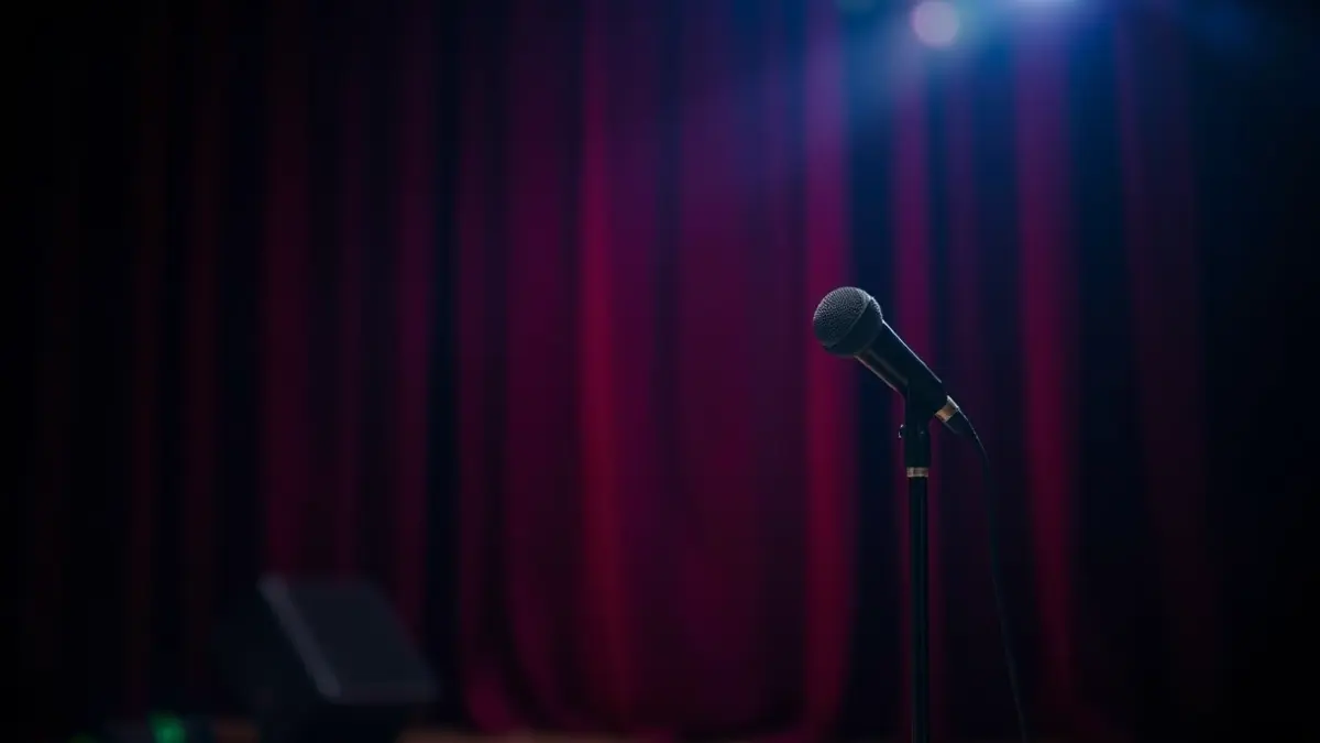 Generic image of a theatrical stage with a microphone and red curtains, with warm lighting.