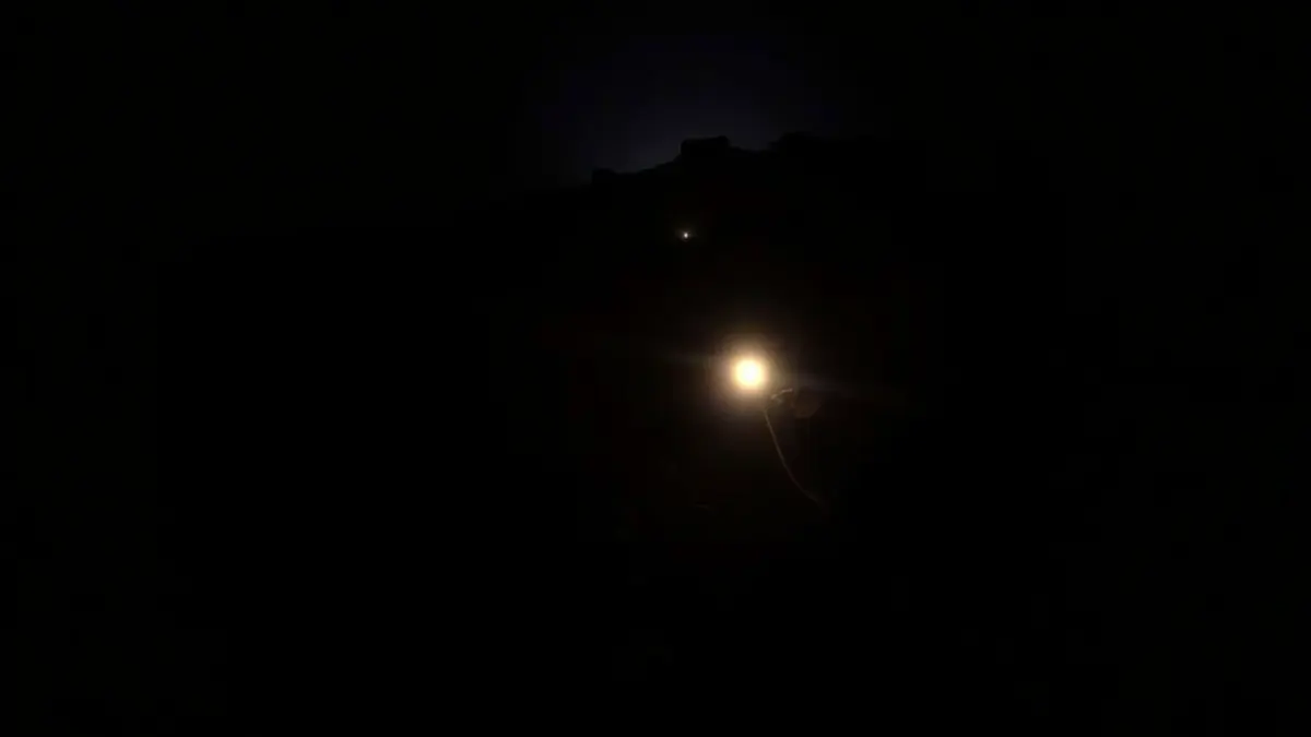 Imatge d'unes llums d'emergència reflectint-se en un camí de muntanya fosc durant la nit, amb siluetes borroses d'arbres.