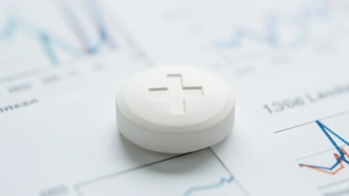 Imatge genèrica d'una pastilla farmacèutica amb un símbol mèdic difuminat al darrere.