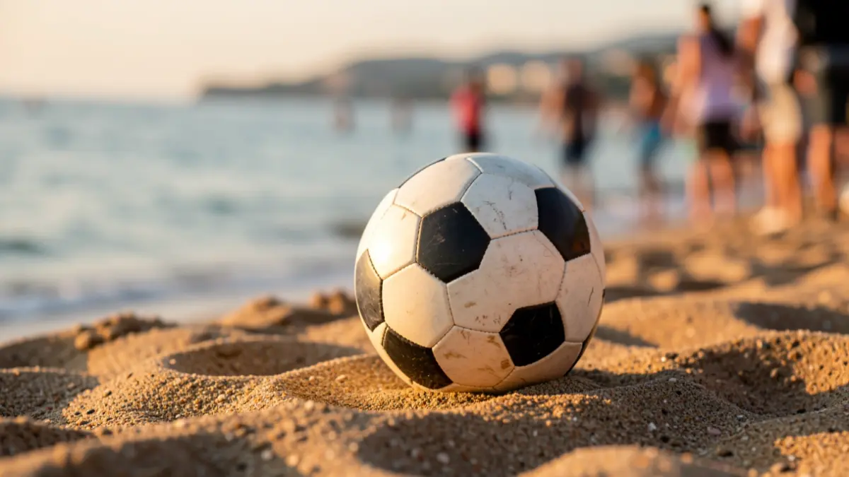 Imagen de un balón de fútbol sobre la arena de la playa con el mar al fondo.