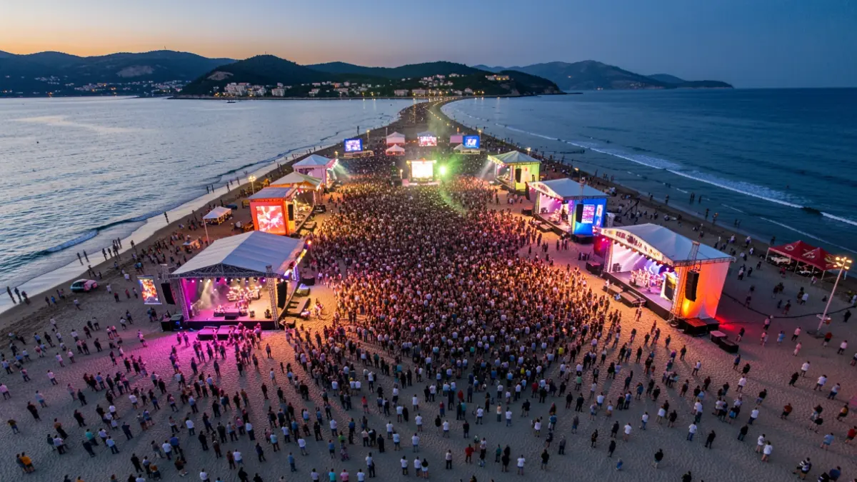 Vista aèria d'un gran festival de música a la platja al capvespre amb múltiples escenaris il·luminats i públic.