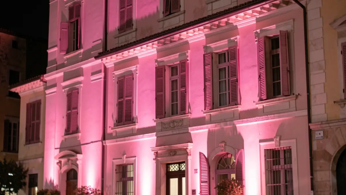 Imatge genèrica d'una façana d'edifici il·luminada de rosa a la nit, simbolitzant la conscienciació sobre el càncer de mama. Il·luminació suau i difosa. Estil arquitectònic mediterrani.